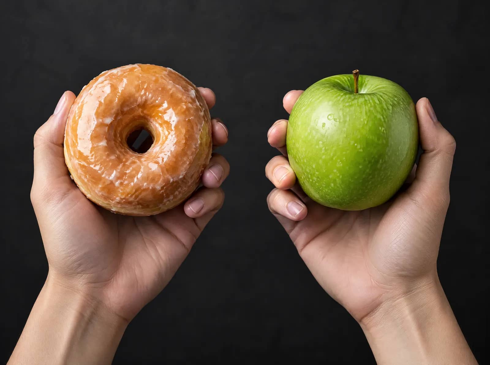 Hands holding a doughnut and a green apple
